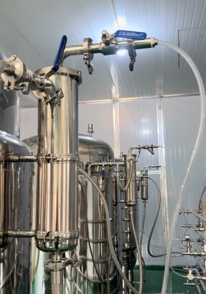 Stainless steel liquid mushroom spawn fermentation system with tanks, pipes, and valves in an industrial facility.