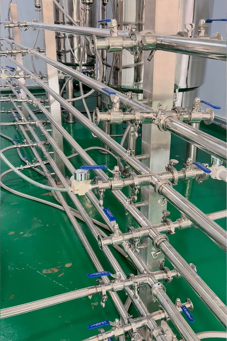 Dense network of stainless steel pipes, blue-handled valves, and fittings on a green industrial floor