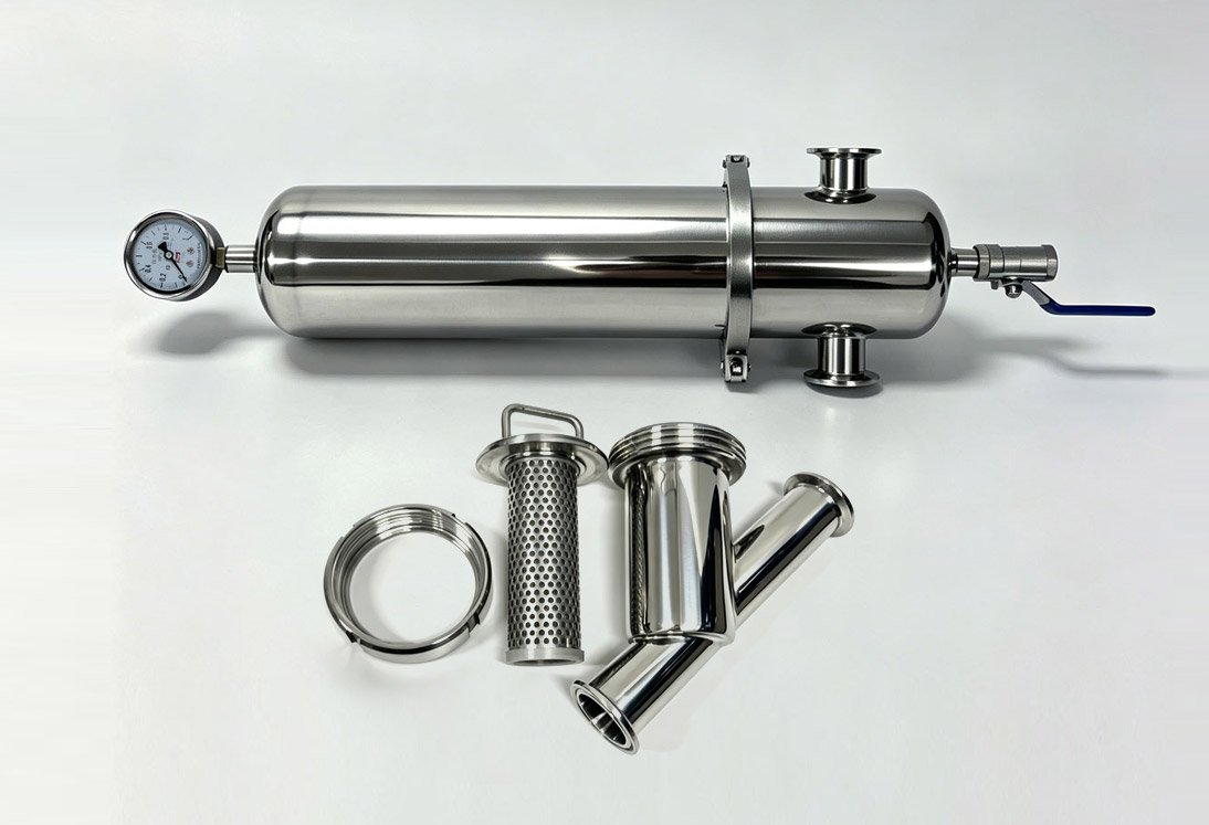 Sanitary stainless steel cartridge filter housing with pressure gauge next to disassembled Y-strainer parts including perforated mesh screen, Tri-Clamp gasket and Y-body for hygienic filtration comparison