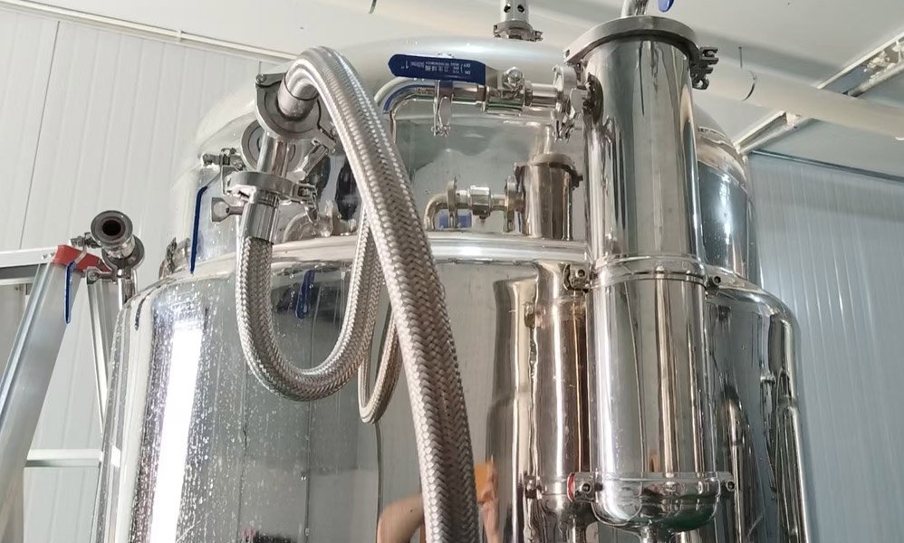 Close-up of a tank breather valve on the upper side of a stainless steel fermentation tank, with polished metal housing, valves, and connected piping