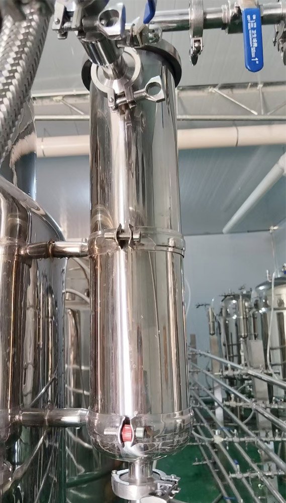 Close-up of a tank breather valve on the upper side of a stainless steel fermentation tank, with polished metal housing, valves, and connected piping