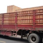Workers loading large wooden export crates and stainless steel tanks onto a red flatbed truck for liquid mushroom spawn production line shipment.