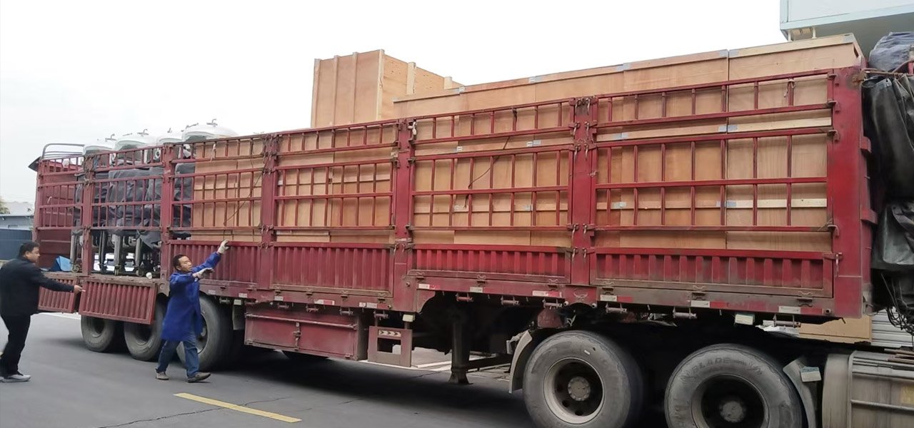 Workers loading large wooden export crates and stainless steel tanks onto a red flatbed truck for liquid mushroom spawn production line shipment.